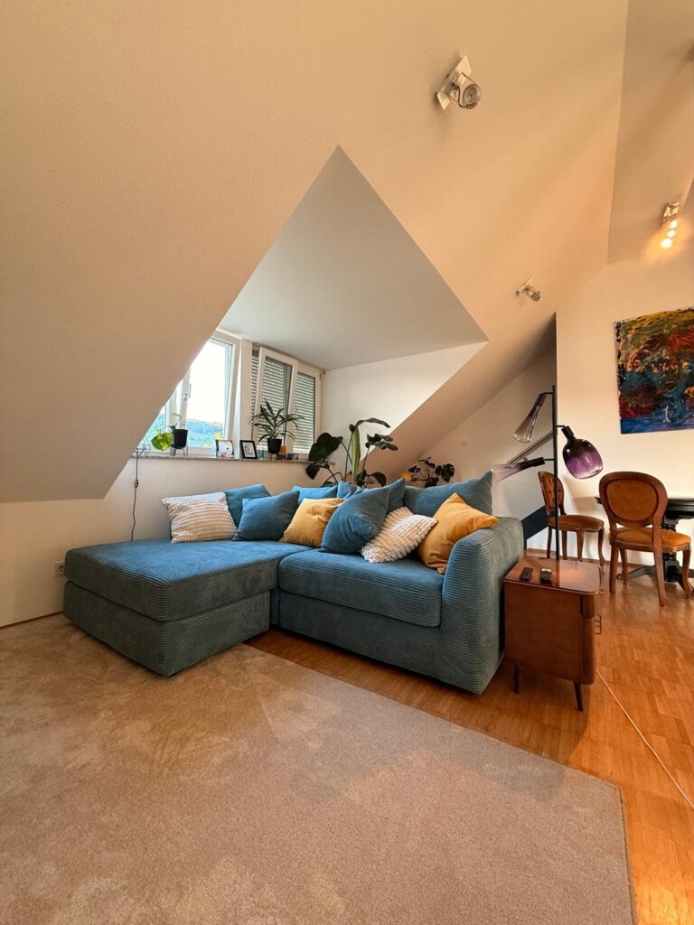Blaues Cordsofa mit Kissen unter einer Dachschraege