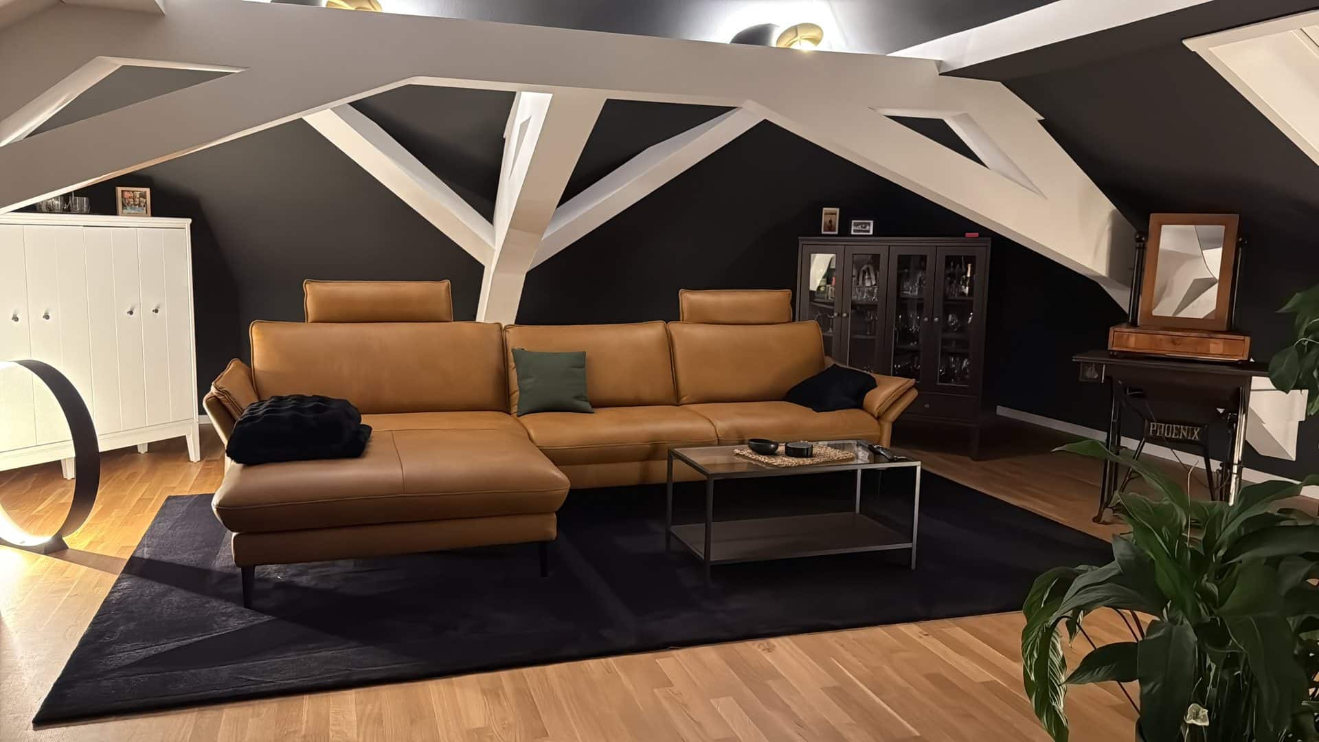 Cognacfarbenes Ledersofa vor dunkler Wand mit sichtbarem Dachstuhl